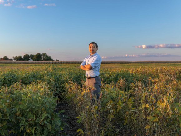 Kaiyu Guan standing in a field with his arms crossed while dressed in business attire