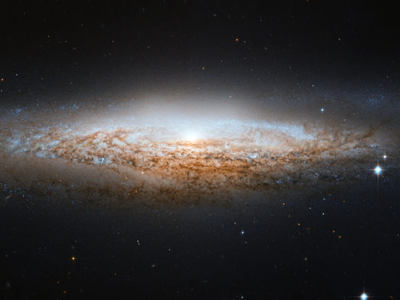 Photograph of a galaxy in outer space surrounded by dust, gas, and stars in gradients and colors of white, yellow, orange, and cyan