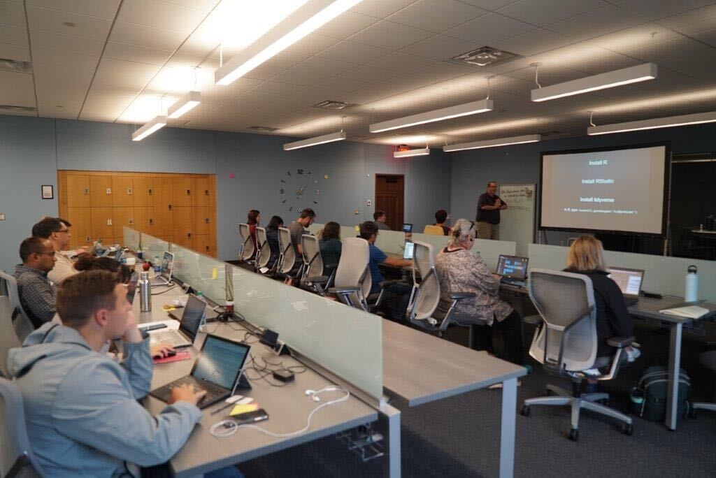 Photograph of a room of two rows of people sitting at laptops during a presentation