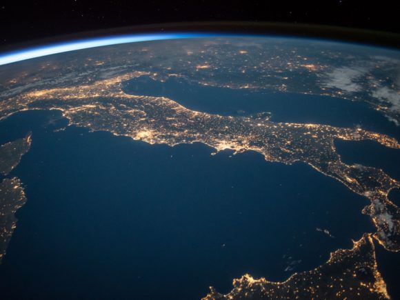 Aerial photograph from space of the world focusing on Italy's landmass and glowing lights indicating larger cities