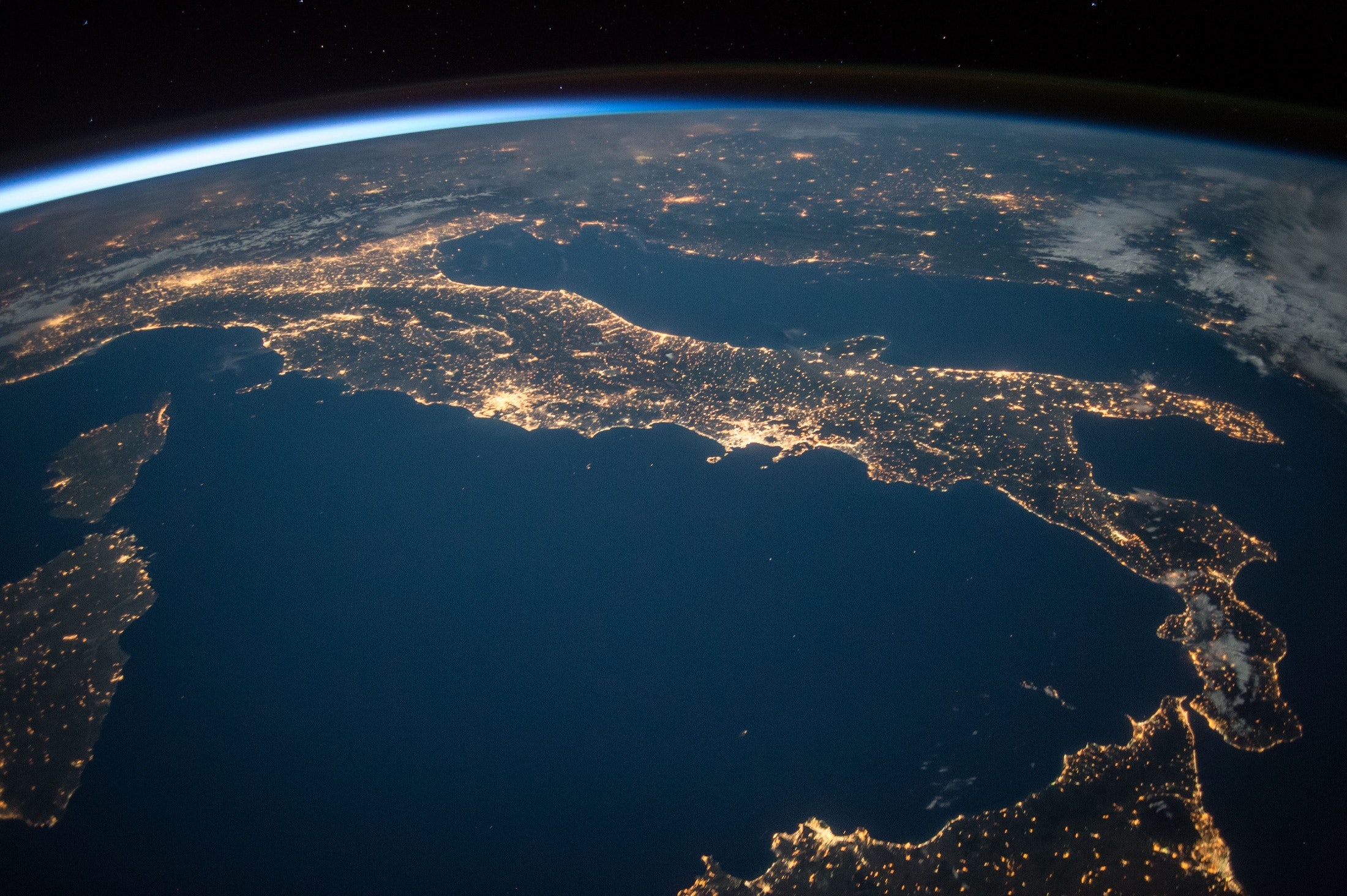 Aerial photograph from space of the world focusing on Italy's landmass and glowing lights indicating larger cities