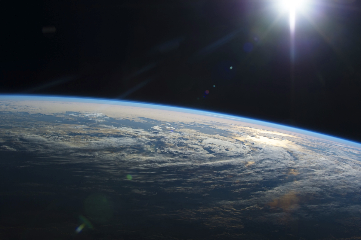 Photograph of Earth's atmosphere from space with the sun shining and creating a lens flare