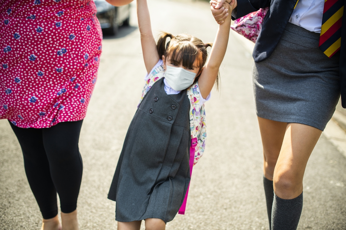 Photograph of a young girl wearing a mask swinging by her arms from two other individuals holder her up as they walk