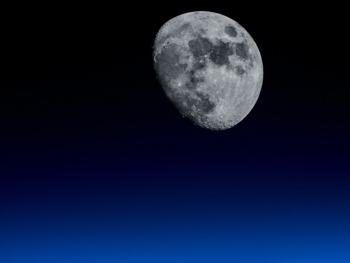 Photograph of a waxing moon with a black to blue atmospheric background