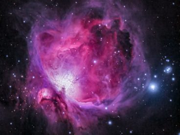 Photograph of the Orion Nebula with gradients of purple, pink, and blue in outer space surrounded by stars