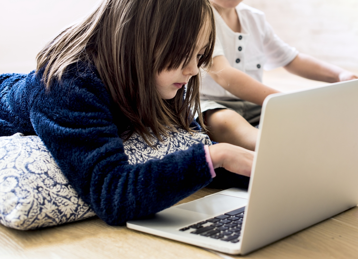 Photograph of a young girl on a laptop with brown hair and a blue sweater