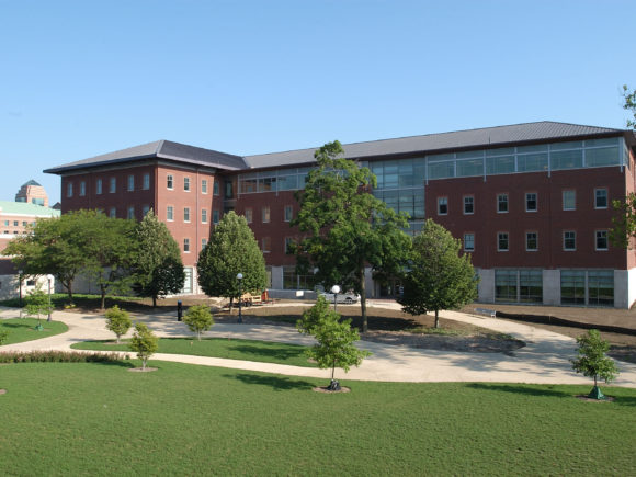 Exterior photograph of the south court yard and entrance of the National Center for Supercomputing Applications. The building is made of red brick, with concrete, and large windows at the top level of the building.