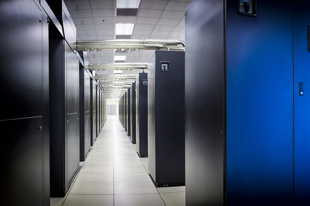 NCSA Blue Waters supercomputer aisle with rows of large black supercomputing cabinets with silver pipes