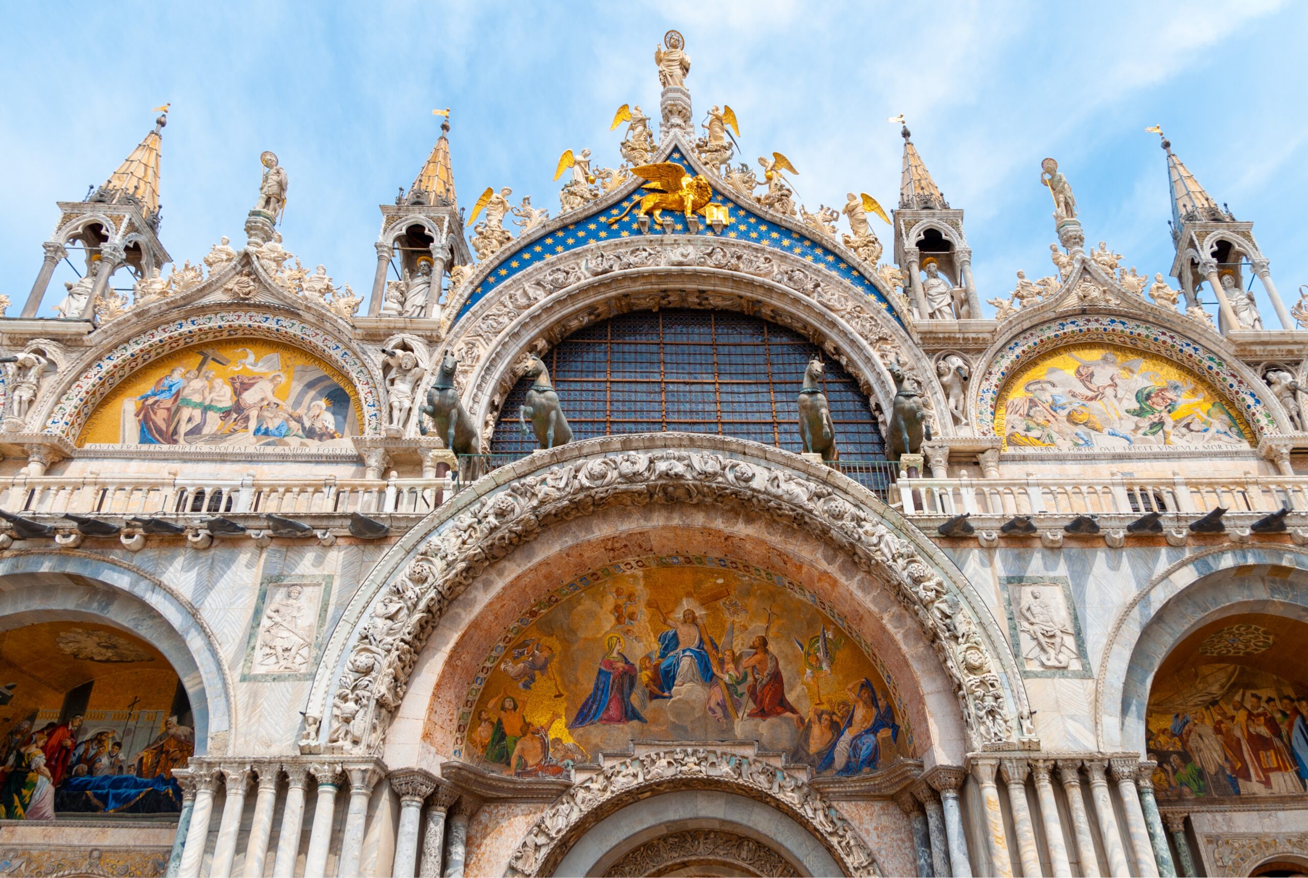 San Marco Basilica in Venice. Ornate statues, arches, and steeples with frescos and gold and blue decoration.