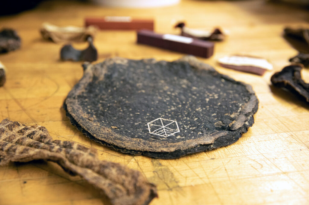 amples of Pyrus material created by Gabe Tavas and Symmetry Wood on a table focused in on a rounded dark sample with the Symmetry Wood logo etched on it.