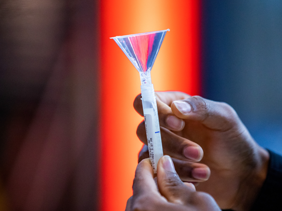 A close up photo of a saliva test tube held by a Black U of I student.