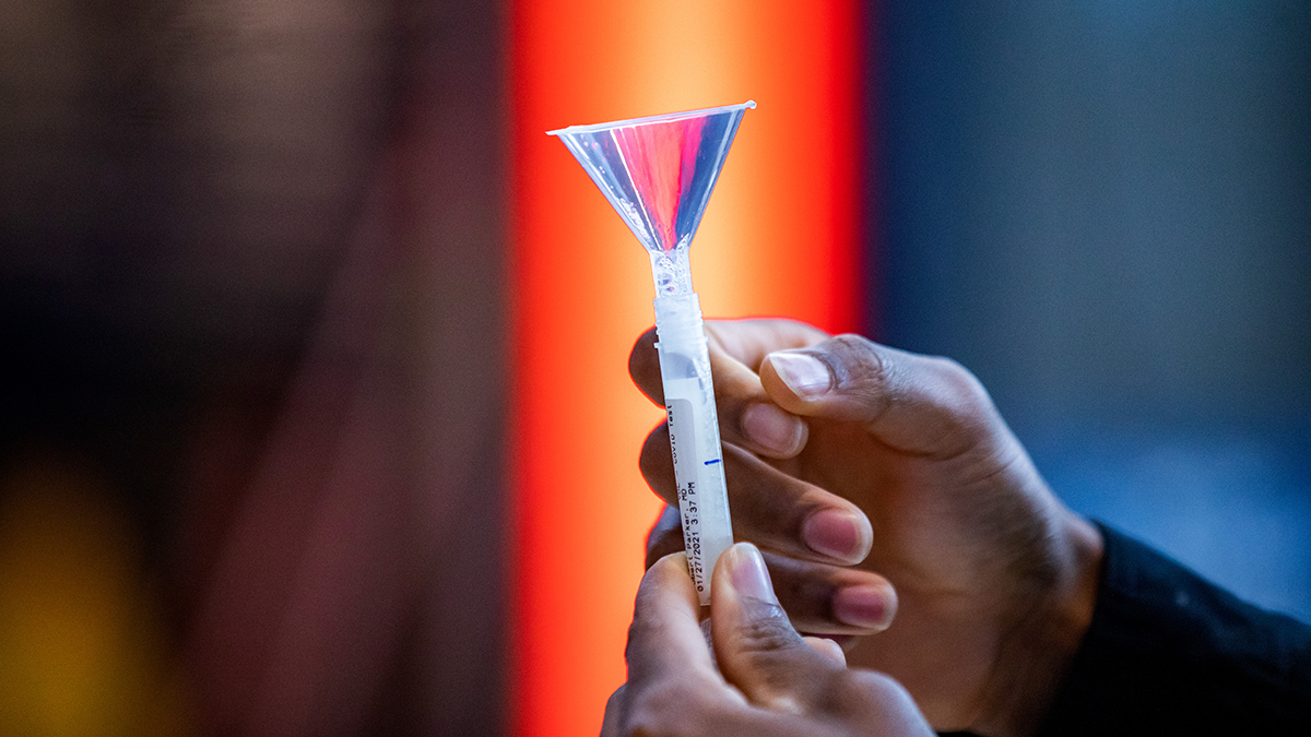 A close up photo of a saliva test tube held by a Black U of I student.