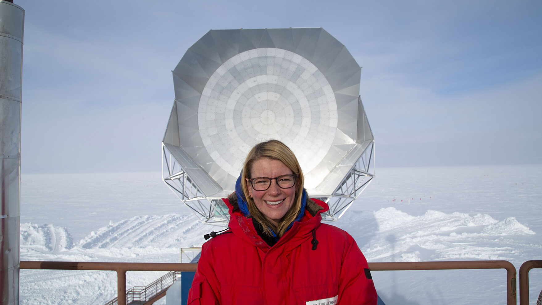 Melanie Archipley standing on the roof of the Dark Sector Lab with a view of the telescope’s primary mirror.