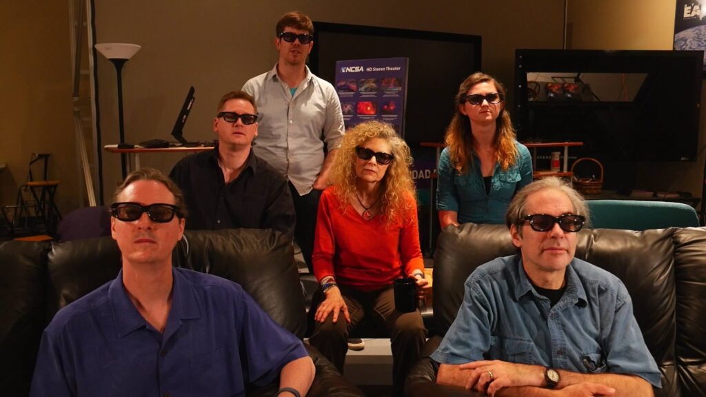Six members of the AVIL team sit facing the camera as if watching a show - they're all wearing 3D glasses.
