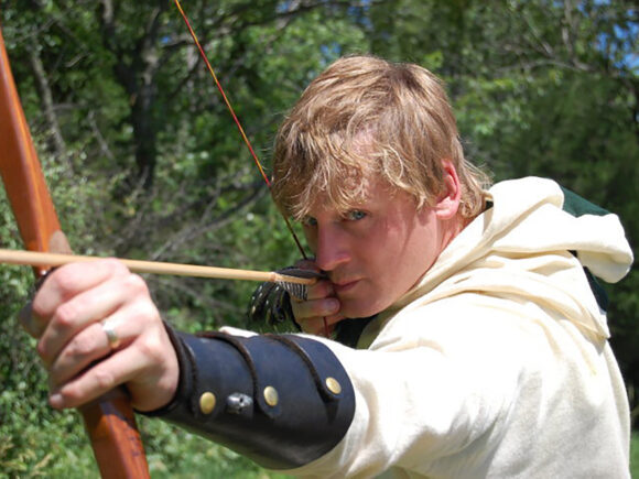 An image of Jeff in an archer costume, holding a bow and arrow, posing as if ready to shoot.