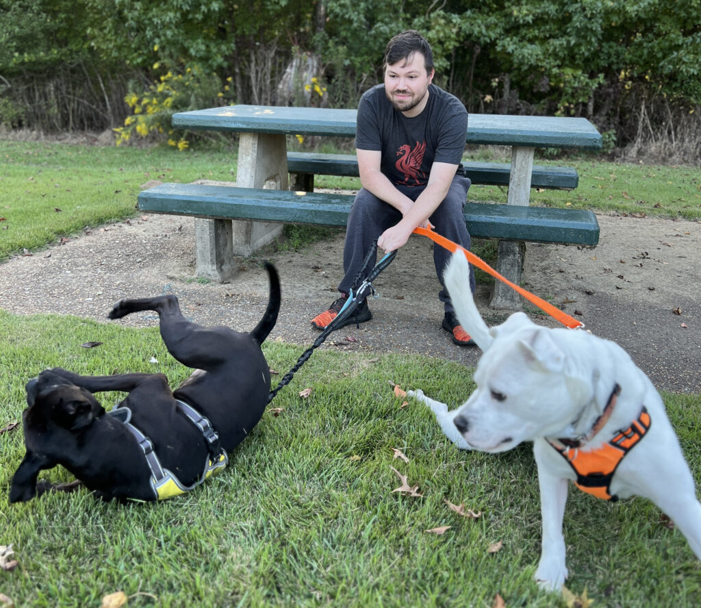 Adam with our two dogs, Aries (on the left) and Falkor (on the right), at a park in Mississippi during a road trip.