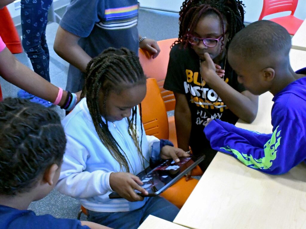 Photo of kids navigating a rover through the classroom using a tablet.