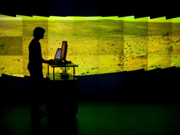 person silhouetted with computer in front of 40-projector display wall at NCSA