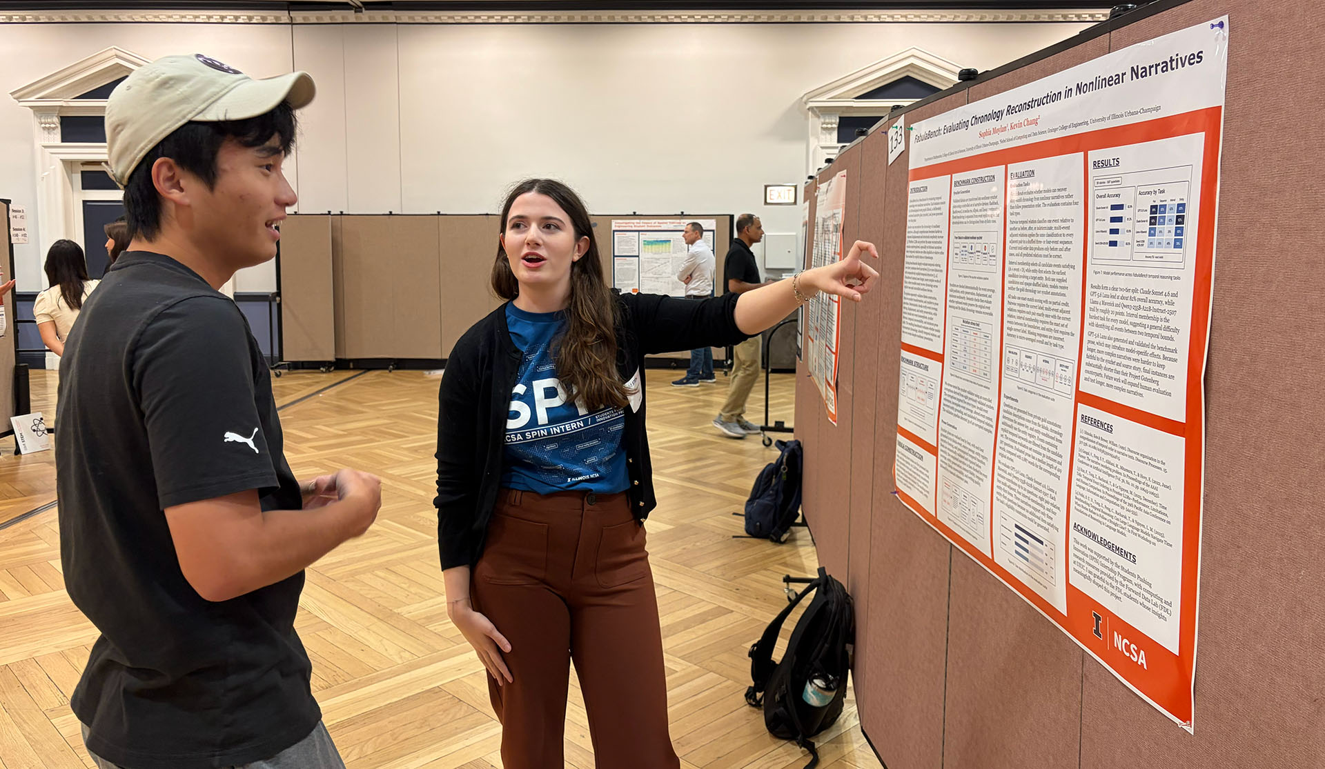 A student shows their poster to a visitor.